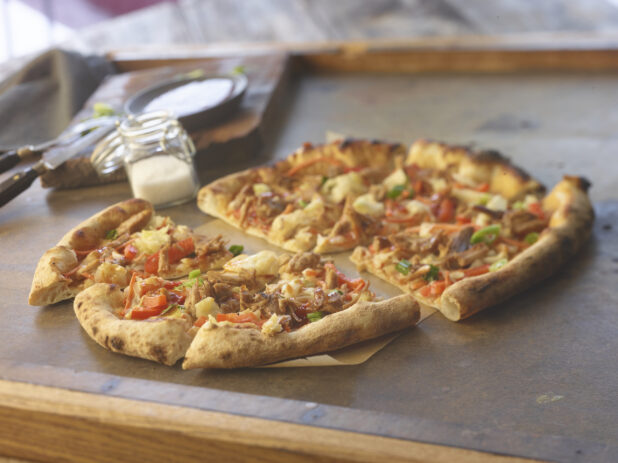 Sliced medium pulled pork pizza with red peppers and onion on parchment paper on a table