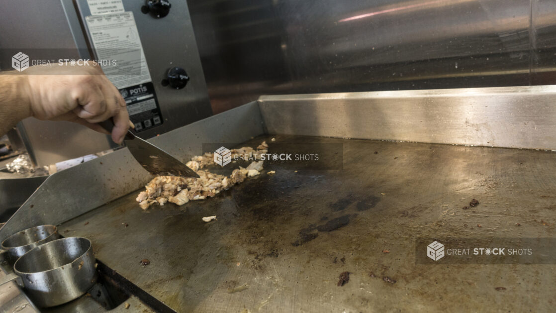 Man cooking chicken on a flat top grill in a restaurant kitchen