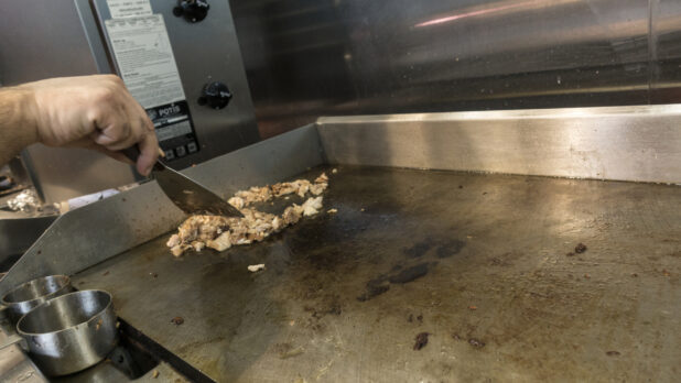 Man cooking chicken on a flat top grill in a restaurant kitchen