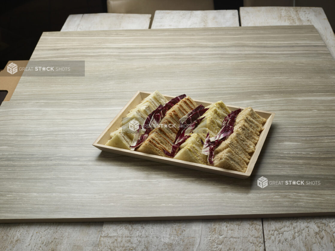 Variety of finger sandwiches on a wooden tray on a wooden background