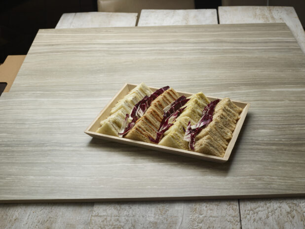 Variety of finger sandwiches on a wooden tray on a wooden background