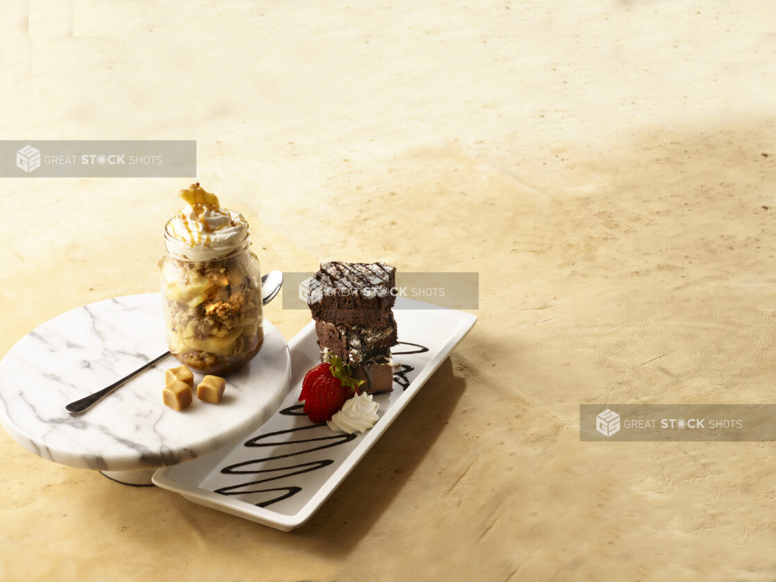 Mason jar of caramel apple crumble and plate of stacked brownies, both garnished with whipped cream