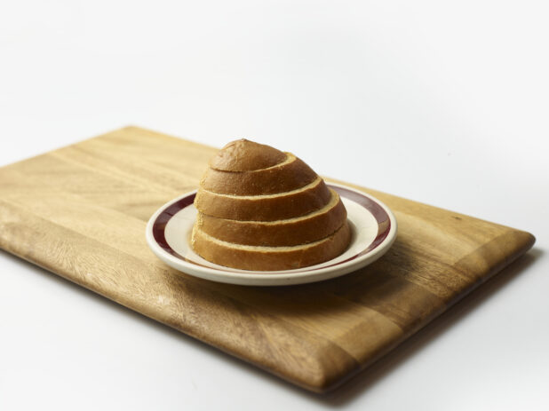 Stack of sliced rye bread on a plate on a wooden board with a white background
