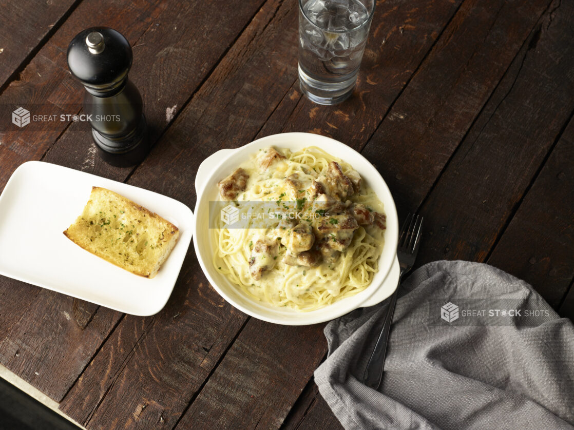 Spaghetti with Alfredo sauce and grilled white meat with a side of garlic bread, white dishes, dark wood background