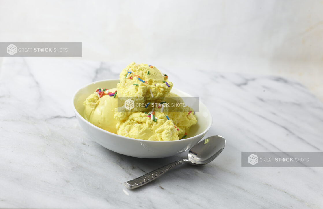 White bowl of French Vanilla ice cream with sprinkles on a white marble background