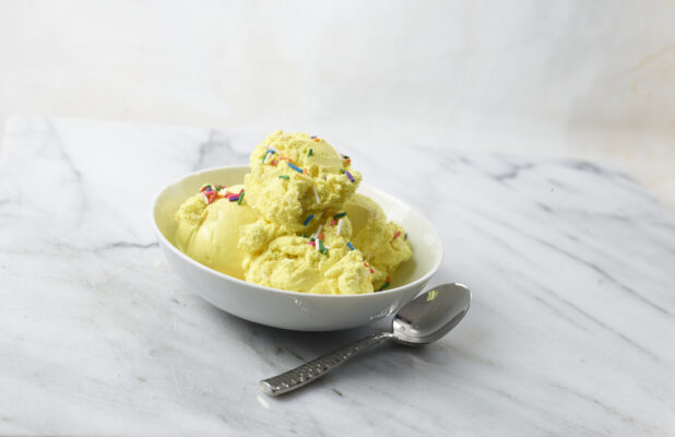 White bowl of French Vanilla ice cream with sprinkles on a white marble background