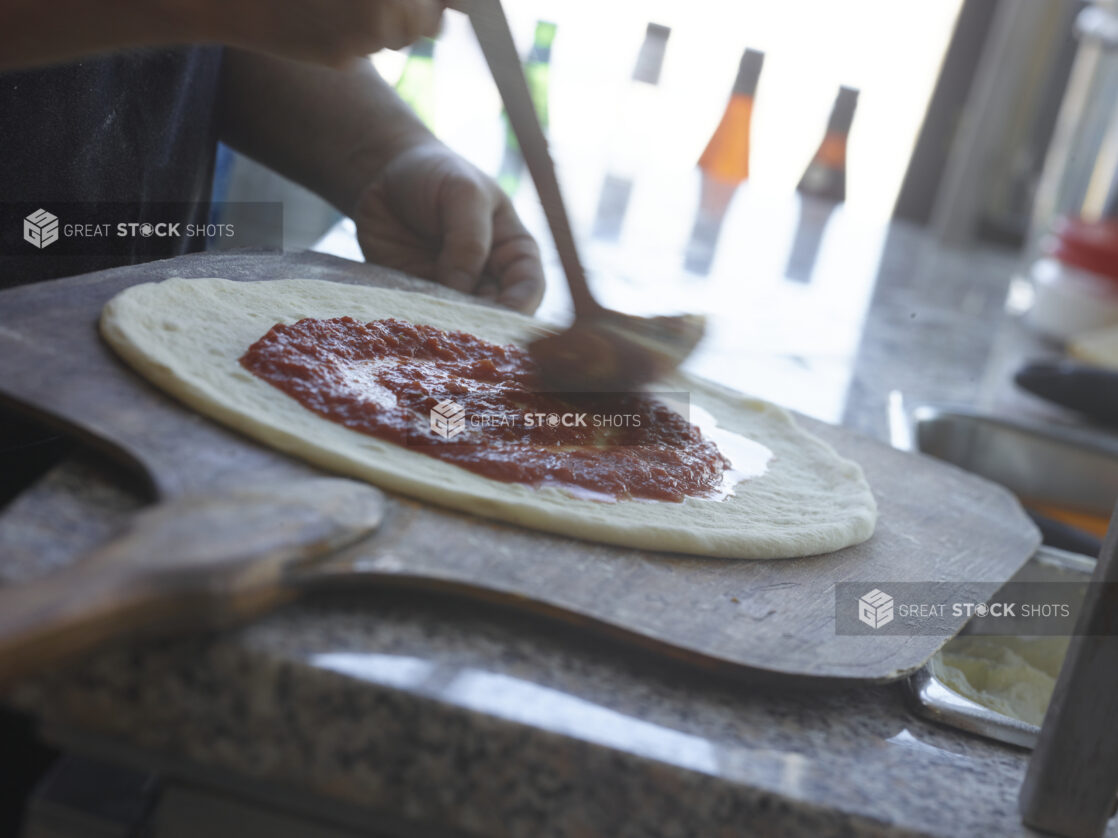 Pizza chef spreading tomato sauce around pizza dough on a peel in a restaurant