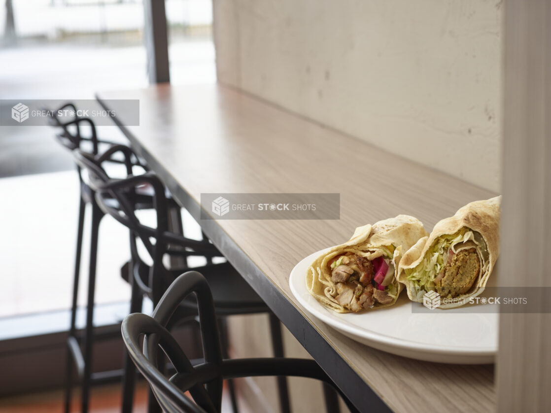 Middle eastern falafel and shawarma pita on a plate sitting on top of a wooden table in a restaurant