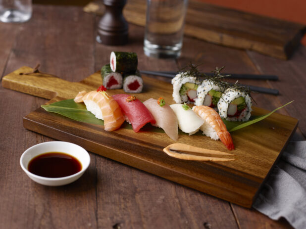 Various sushi and maki rolls on a wooden cutting board with chopsticks