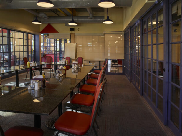 Large empty meeting space in a restaurant with red chairs and paned glass walls