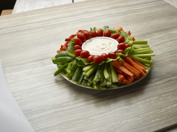 Large vegetable platter with creamy dip in the center on a wooden background