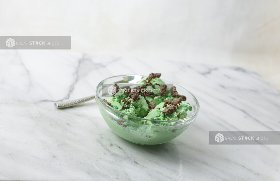 Mint ice cream topped with chocolate cookie crumble and chocolate sprinkles on a white marble background