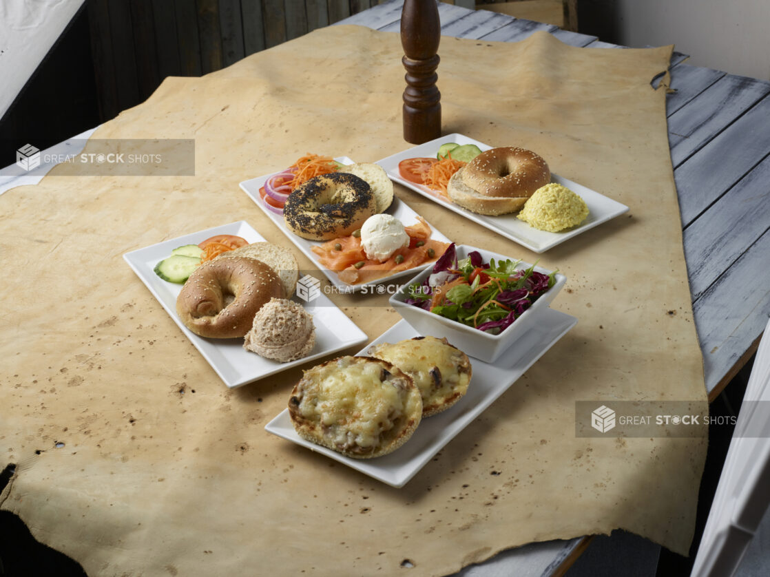 Various breakfast / brunch plates with bagels, toppings, smears and a side salad on a light background