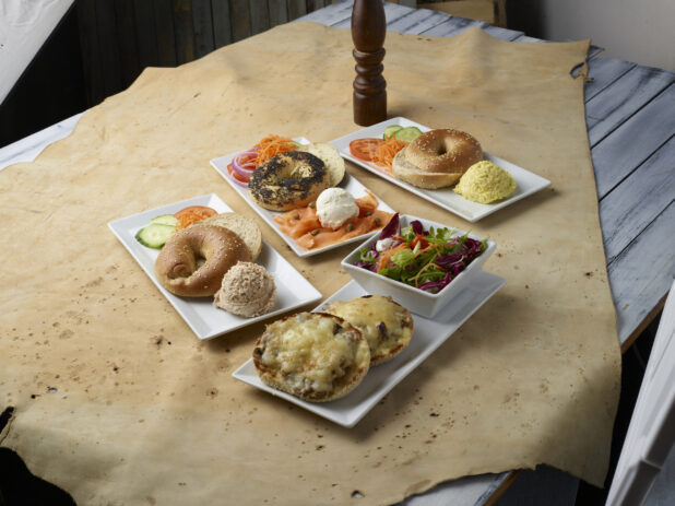 Various breakfast / brunch plates with bagels, toppings, smears and a side salad on a light background