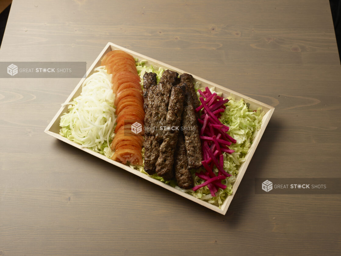 Overhead view of a wooden platter with sliced, onion, tomatoes, turnip and beef kebab on a wooden background