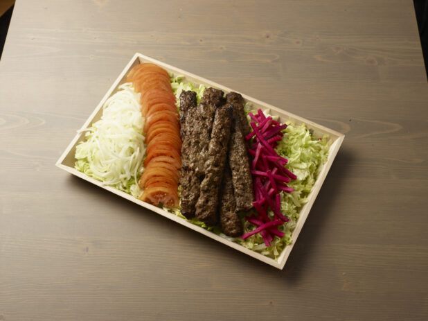 Overhead view of a wooden platter with sliced, onion, tomatoes, turnip and beef kebab on a wooden background