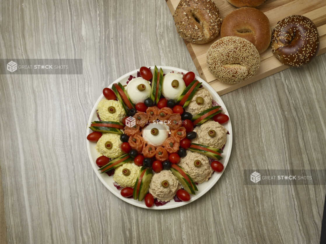 Overhead of various schmears and toppings with bagels in the background on a wooden background