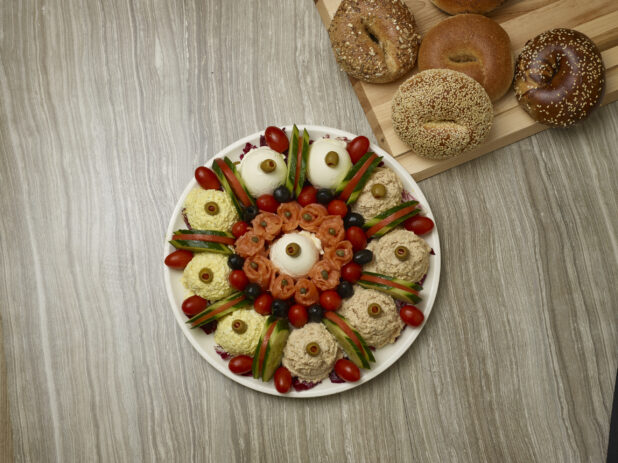 Overhead of various schmears and toppings with bagels in the background on a wooden background