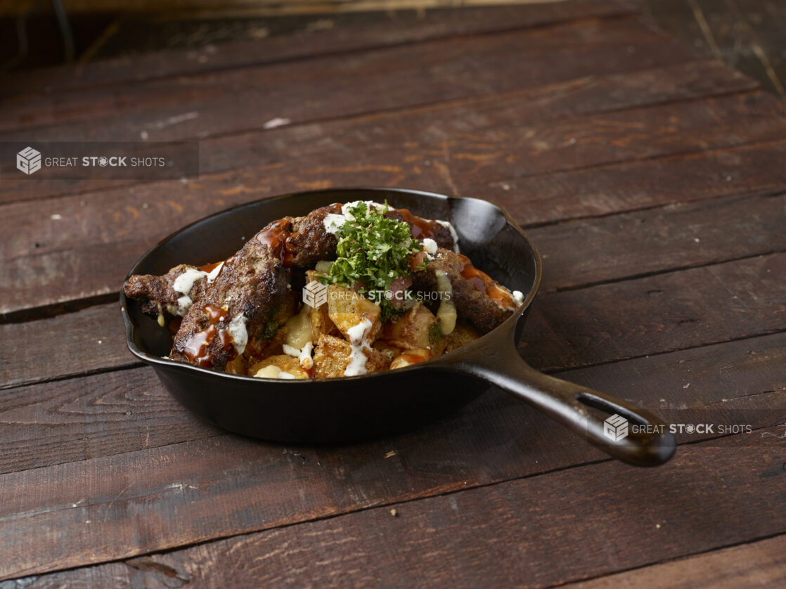 Beef kebab potato skillet topped with tabouli on dark wood background