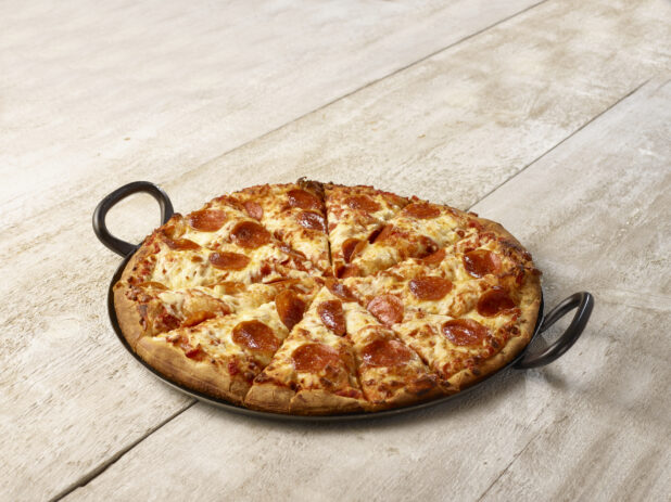 Sliced pepperoni pizza in a black cast iron pan on a wooden background