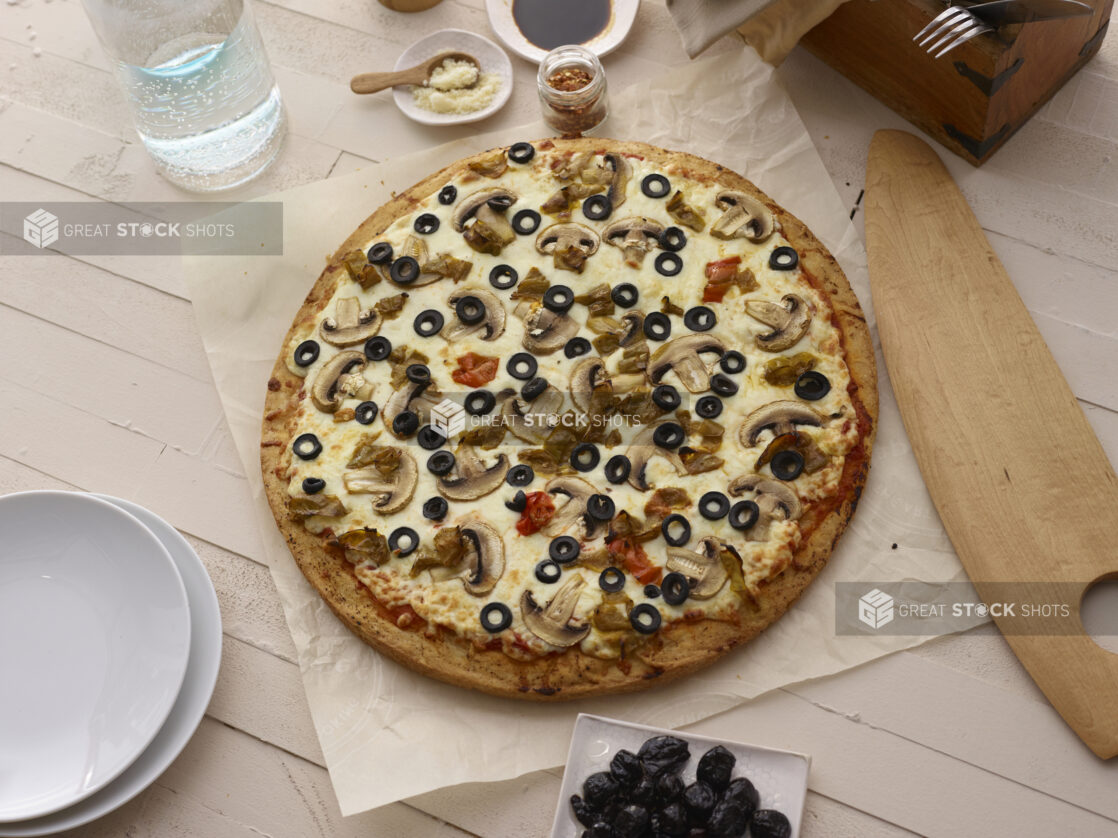 Whole vegetarian pizza on parchment with a white washed wooden background