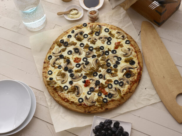 Whole vegetarian pizza on parchment with a white washed wooden background