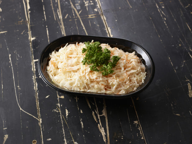 Black bowl of vinaigrette coleslaw garnished with parsley on a distressed black wooden background