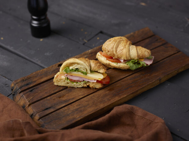 Ham and cheese croissant sandwich cut in half on a wooden board
