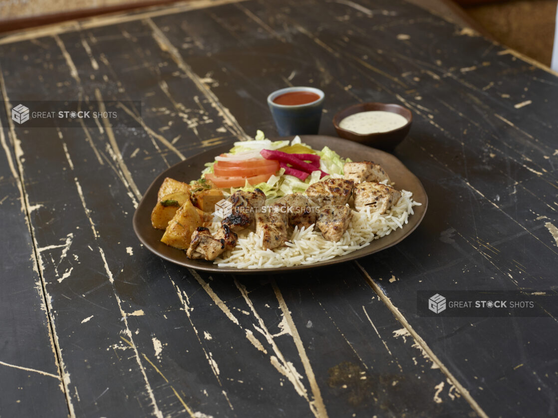 Middle eastern platter with chicken souvlaki, rice, potatoes and salad with sauces on a distressed wooden background