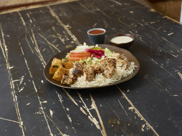 Middle eastern platter with chicken souvlaki, rice, potatoes and salad with sauces on a distressed wooden background