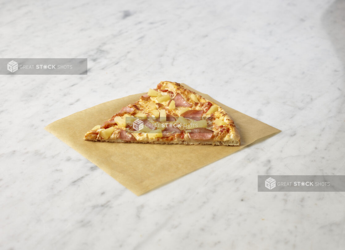 Hawaiian pizza slice on parchment paper on a marble background