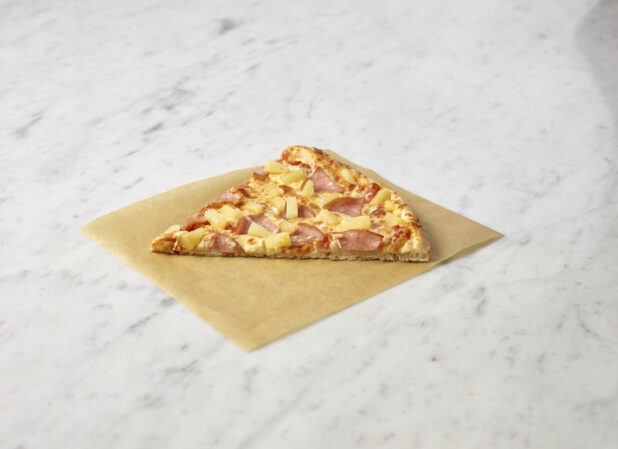 Hawaiian pizza slice on parchment paper on a marble background