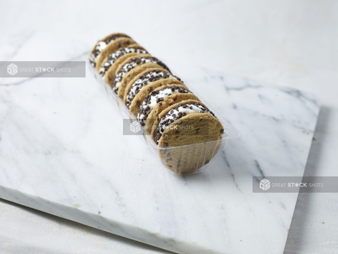 Chocolate chip cookie ice cream sandwiches in a plastic container on a marble slab