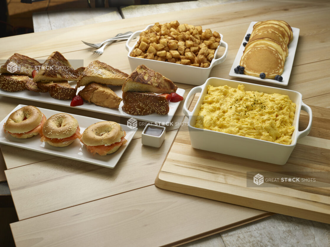 Buffet breakfast, brunch of lox and cream cheese bagels, scrambled eggs, pancakes, home fries and french toast on a wooden background