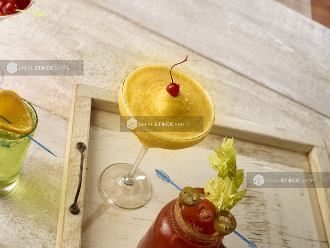 Tropical margarita with maraschino cherry garnish with other cocktails on wooden serving tray