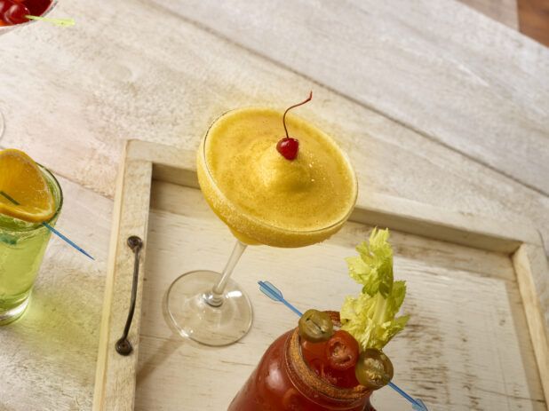 Tropical margarita with maraschino cherry garnish with other cocktails on wooden serving tray