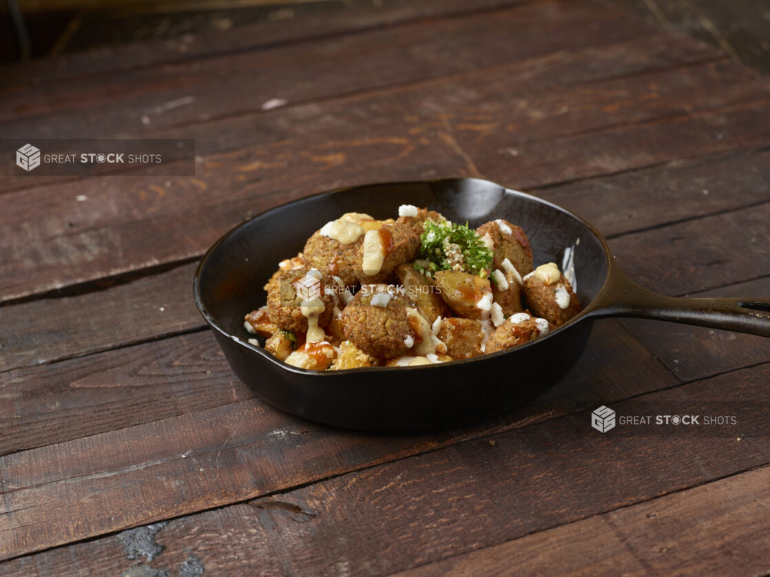 Falafel, potato in a black iron skillet topped with tabouli on dark wood background