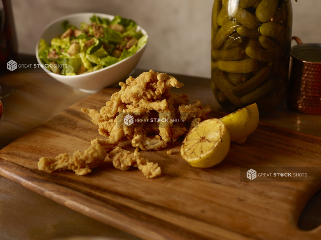 Fried calamari and grilled lemon on a wooden board with a bowl of salad in behind