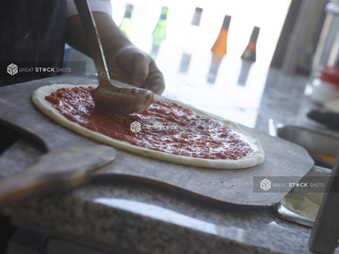 Pizza chef spreading tomato sauce around pizza dough on a peel in a restaurant