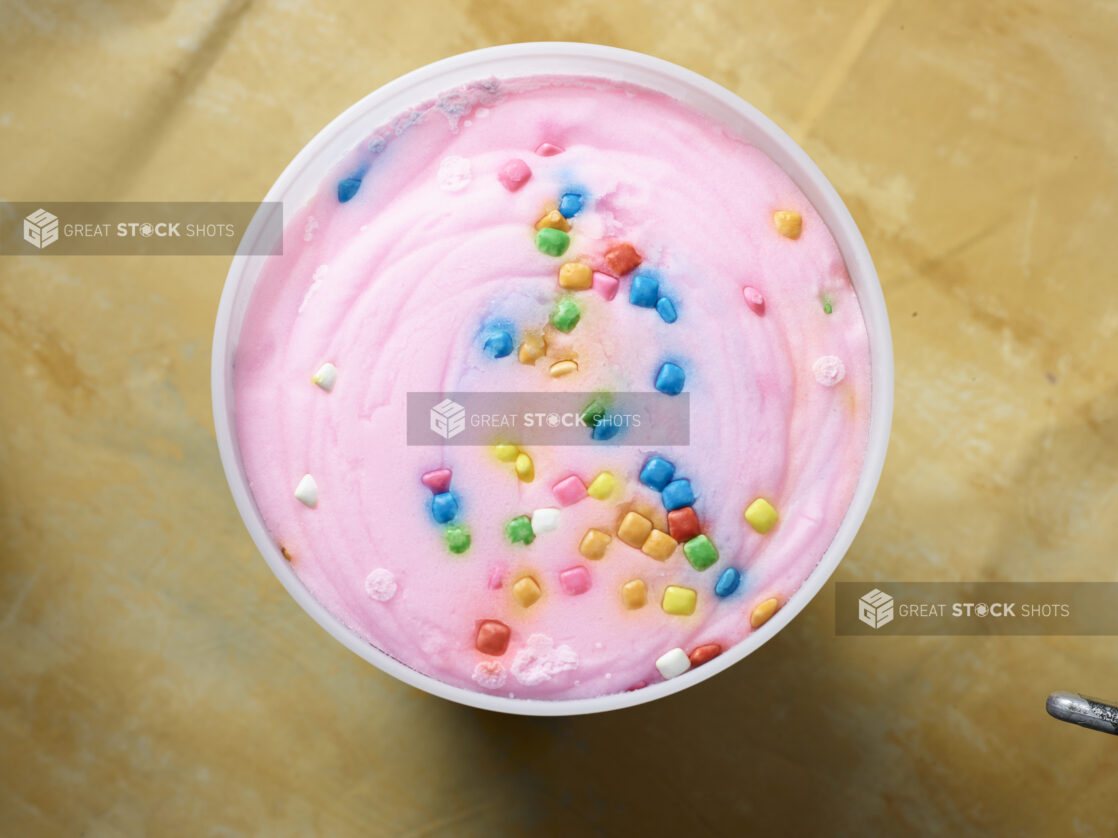 Overhead view of a large tub of bubble gum ice cream / gelato on a yellow background