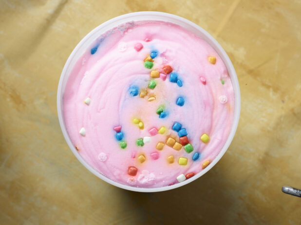 Overhead view of a large tub of bubble gum ice cream / gelato on a yellow background
