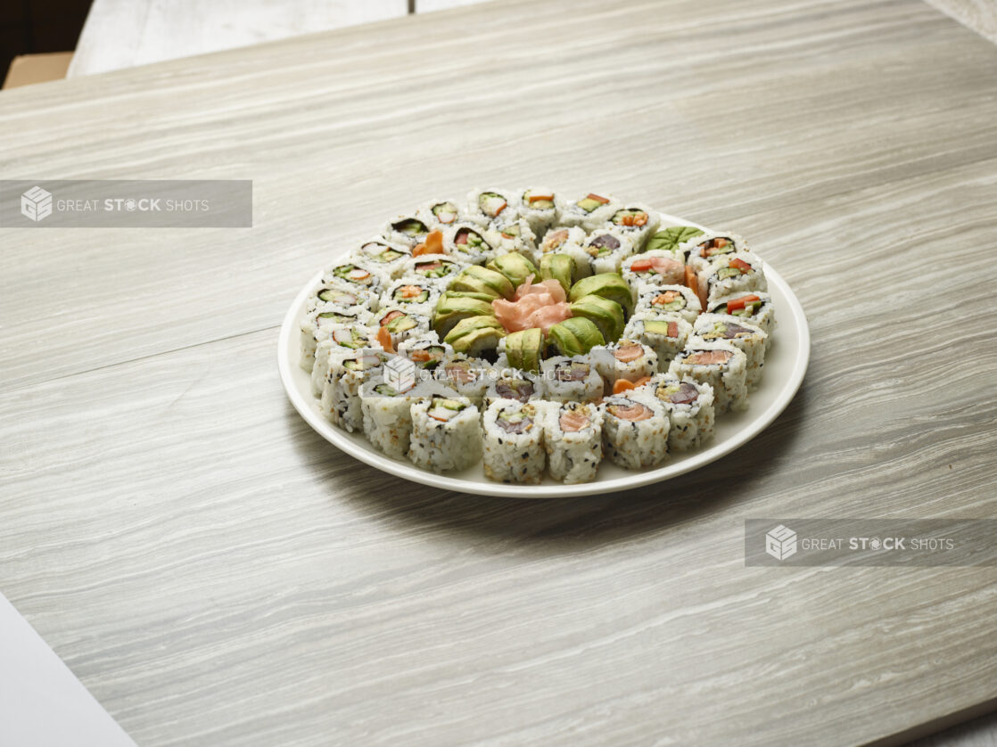 Platter of assorted maki rolls with fresh pink ginger in the middle of a white plate on a wooden background