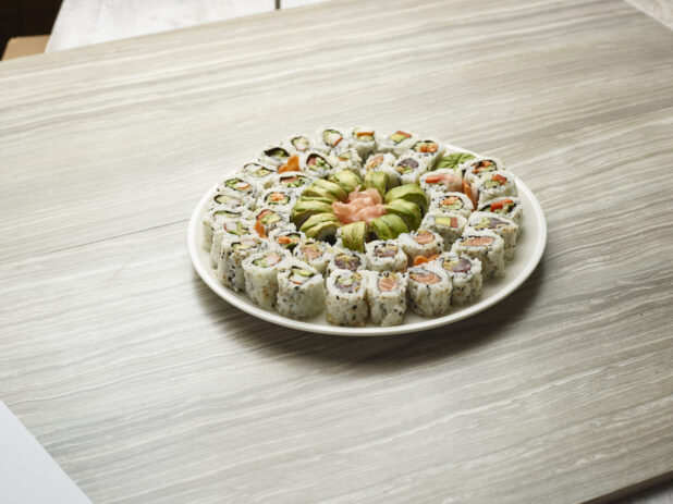 Platter of assorted maki rolls with fresh pink ginger in the middle of a white plate on a wooden background