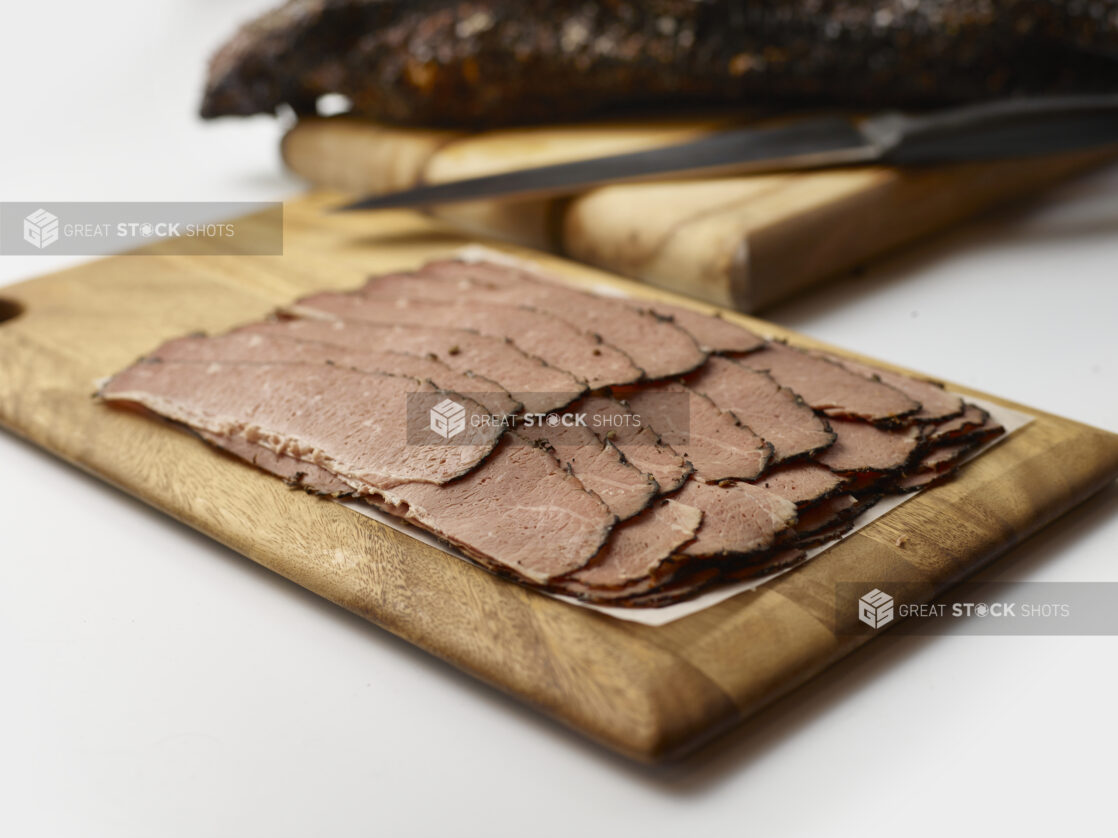 Thin slices of roast beef layered on parchment paper on a wooden board, white background