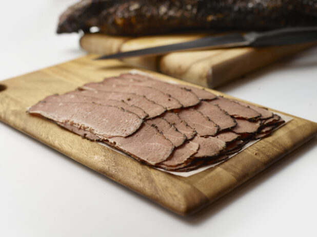 Thin slices of roast beef layered on parchment paper on a wooden board, white background