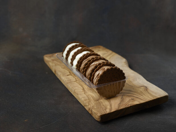 Vanilla and chocolate ice cream sandwiches in a plastic container on a wooden board on a dark background