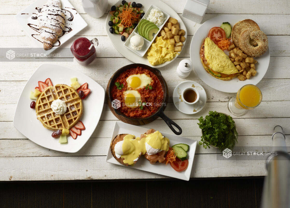 Overhead of various breakfast / brunch dishes on white plates on a white washed wooden background