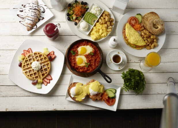 Overhead of various breakfast / brunch dishes on white plates on a white washed wooden background