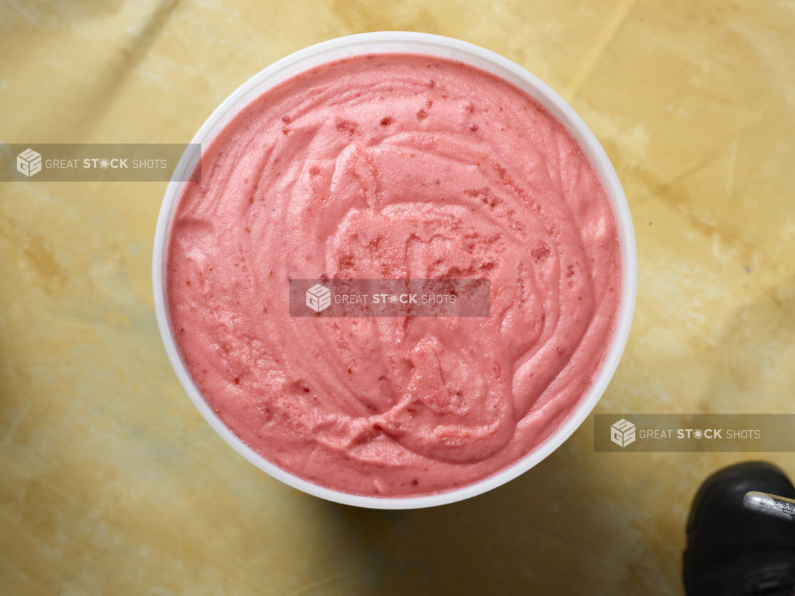 Overhead view of a large tub of berry ice cream / gelato on a yellow background