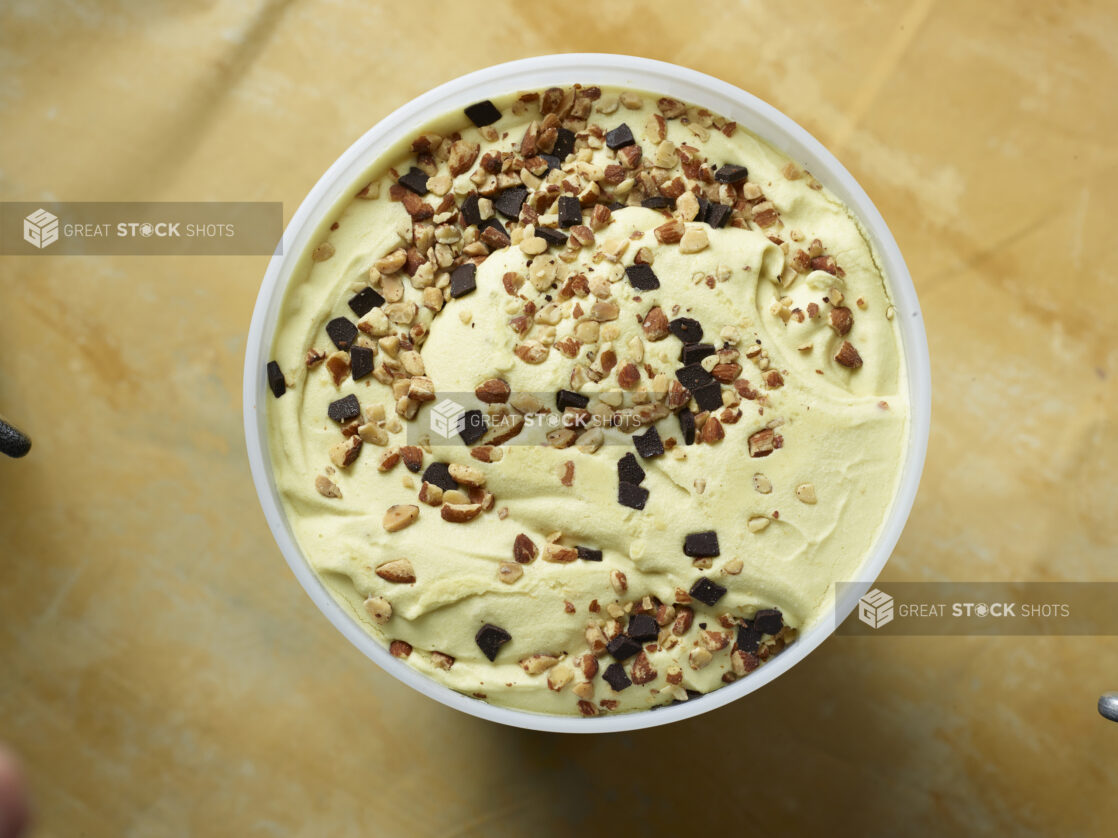 Overhead view of a large tub of vanilla chocolate chip almond ice cream on a yellow background